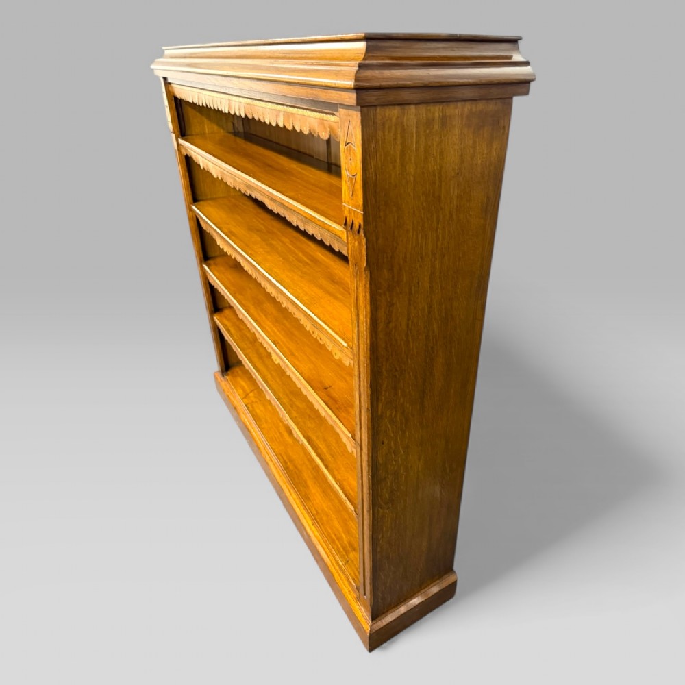A late Victorian open bookcase crafted from golden oak, featuring scalloped edging along each shelf and subtle geometric carvings on the pilasters. View VI