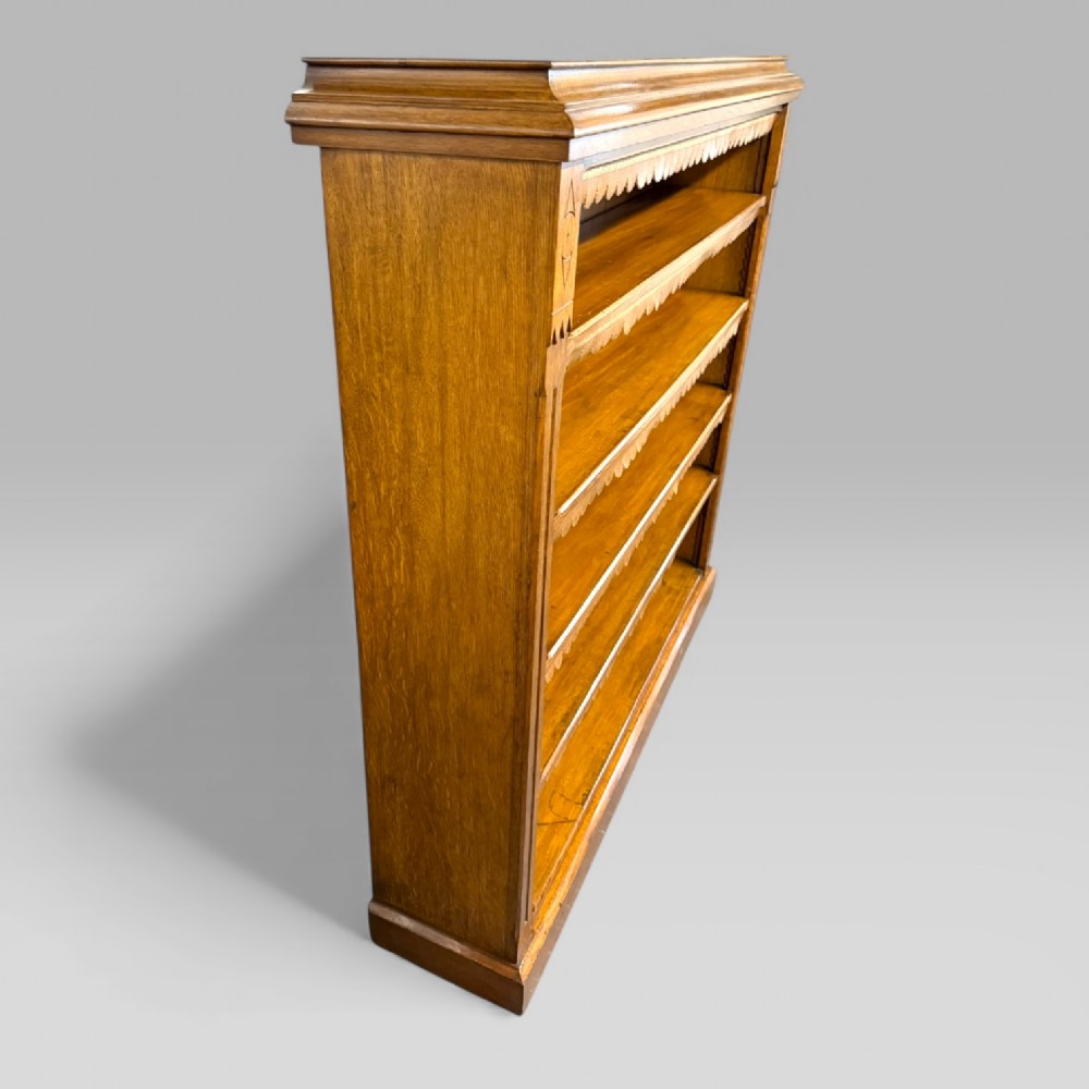 A late Victorian open bookcase crafted from golden oak, featuring scalloped edging along each shelf and subtle geometric carvings on the pilasters. View VII