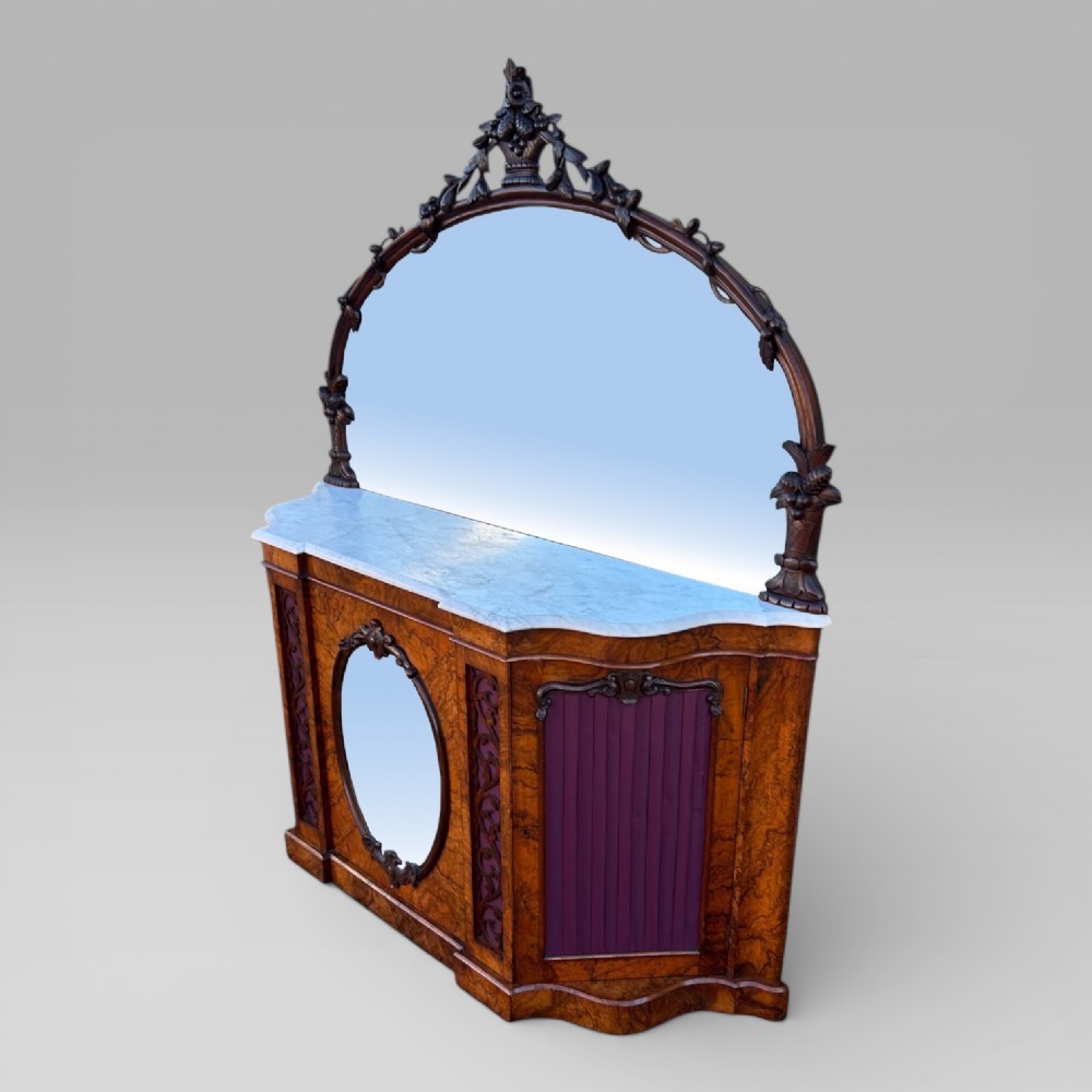 A Victorian walnut credenza featuring a breakfront white marble top, an arched crest-carved mirror frame, and base panels detailed with an oval mirror and fabric behind fretwork. View III