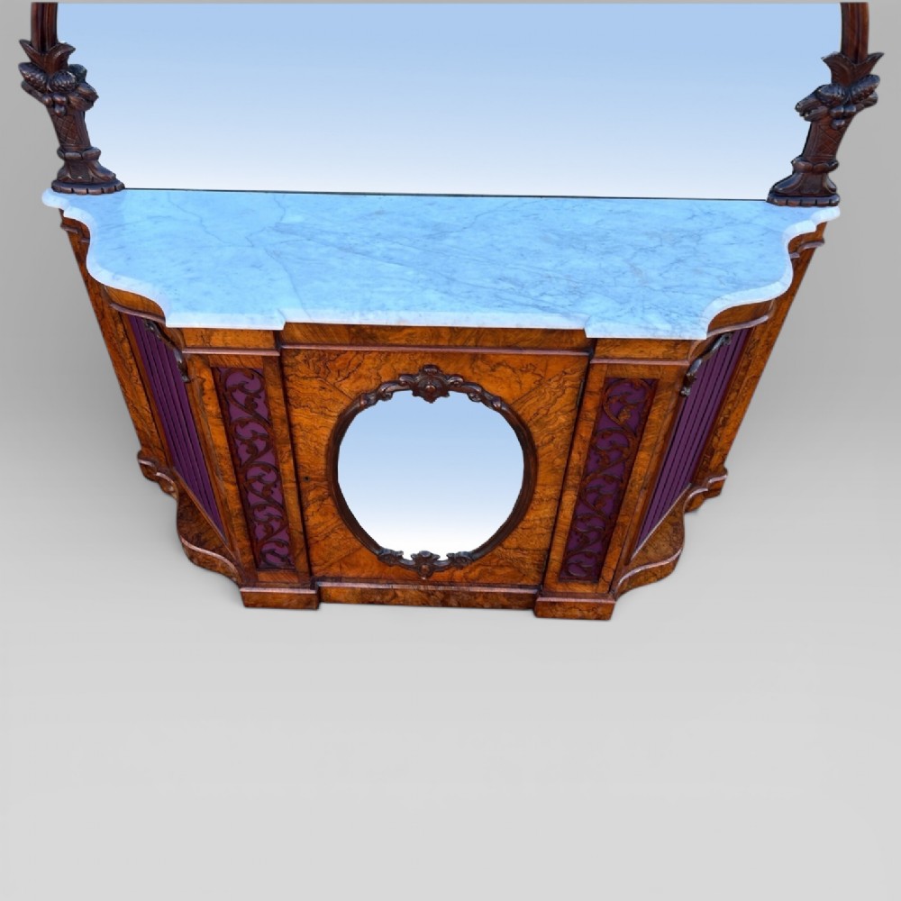A Victorian walnut credenza featuring a breakfront white marble top, an arched crest-carved mirror frame, and base panels detailed with an oval mirror and fabric behind fretwork. View IV
