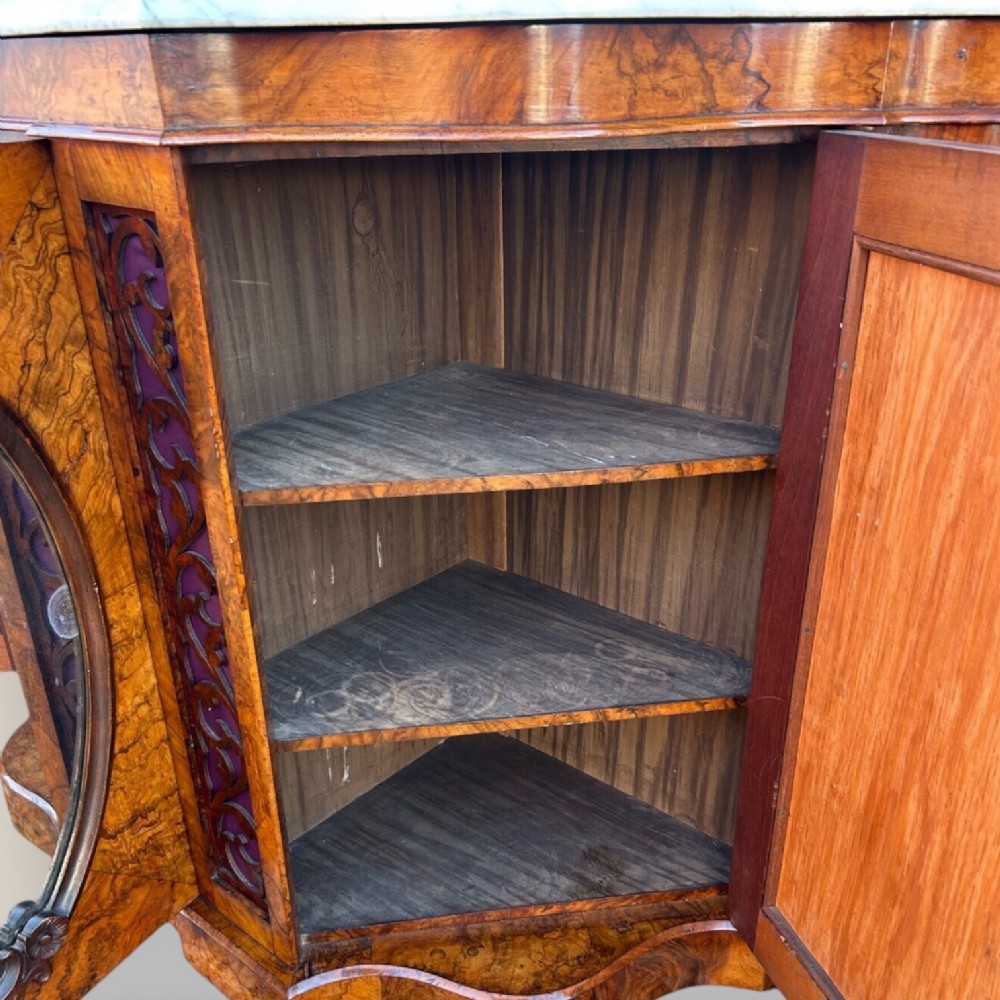 A Victorian walnut credenza featuring a breakfront white marble top, an arched crest-carved mirror frame, and base panels detailed with an oval mirror and fabric behind fretwork. View IX
