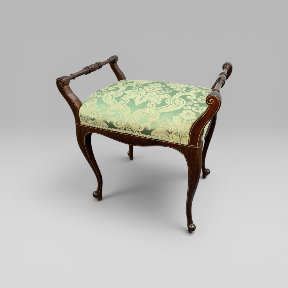 An antique mahogany piano stool featuring cabriole legs, fine line inlay, turned handles, and green floral damask upholstered seating.