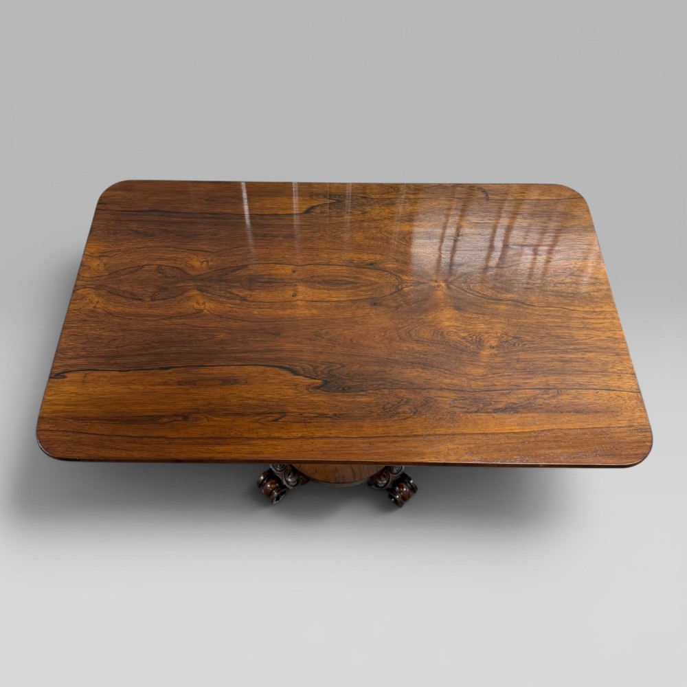 An antique William IV rosewood centre table featuring a rectangular top with rounded corners resting on a central turned pedestal and carved feet. View IV