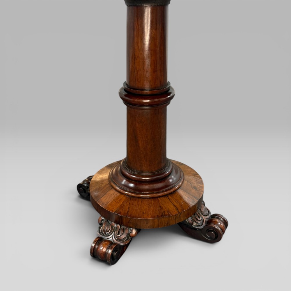 An antique William IV rosewood centre table featuring a rectangular top with rounded corners resting on a central turned pedestal and carved feet. View VI