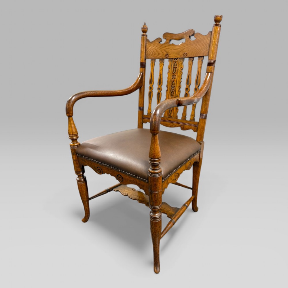 A Victorian carved golden oak armchair featuring a pierced vertical slat backrest, sculpted armrests, turned legs, and a brown leather seat.