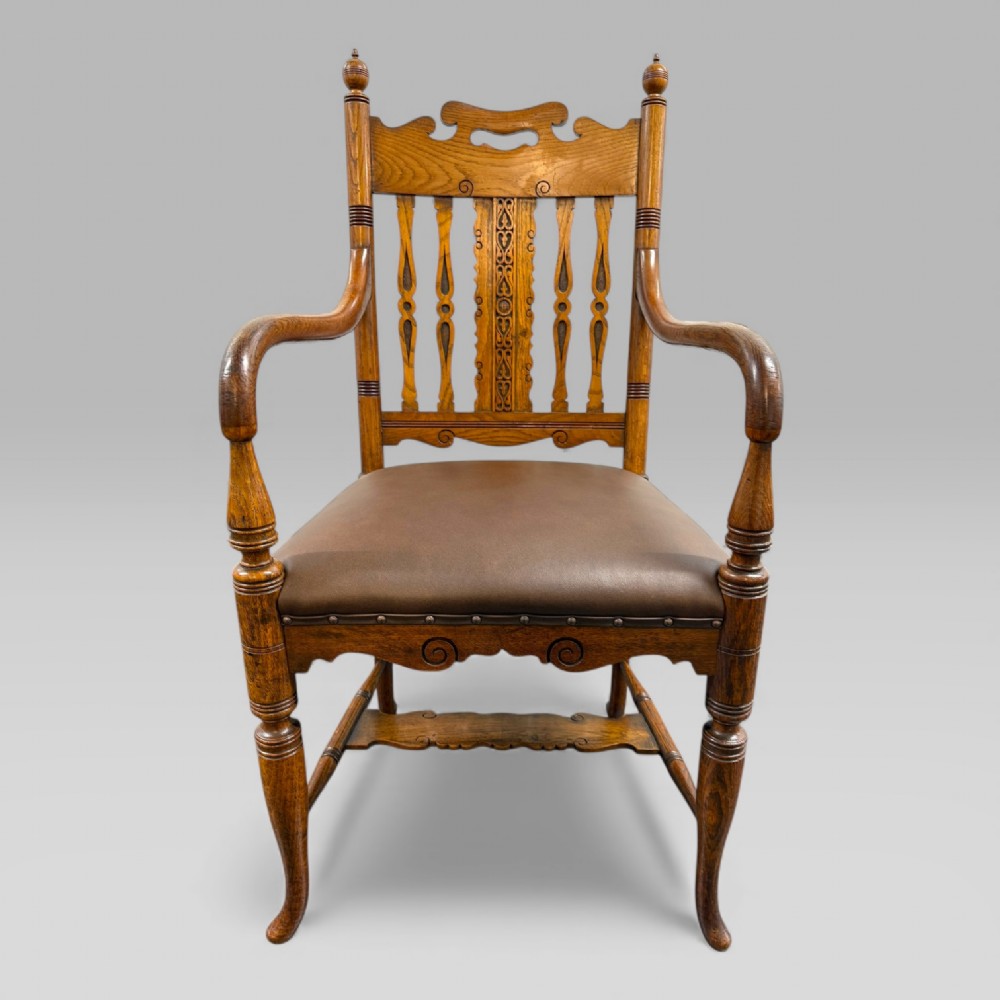 A Victorian carved golden oak armchair featuring a pierced vertical slat backrest, sculpted armrests, turned legs, and a brown leather seat. View II