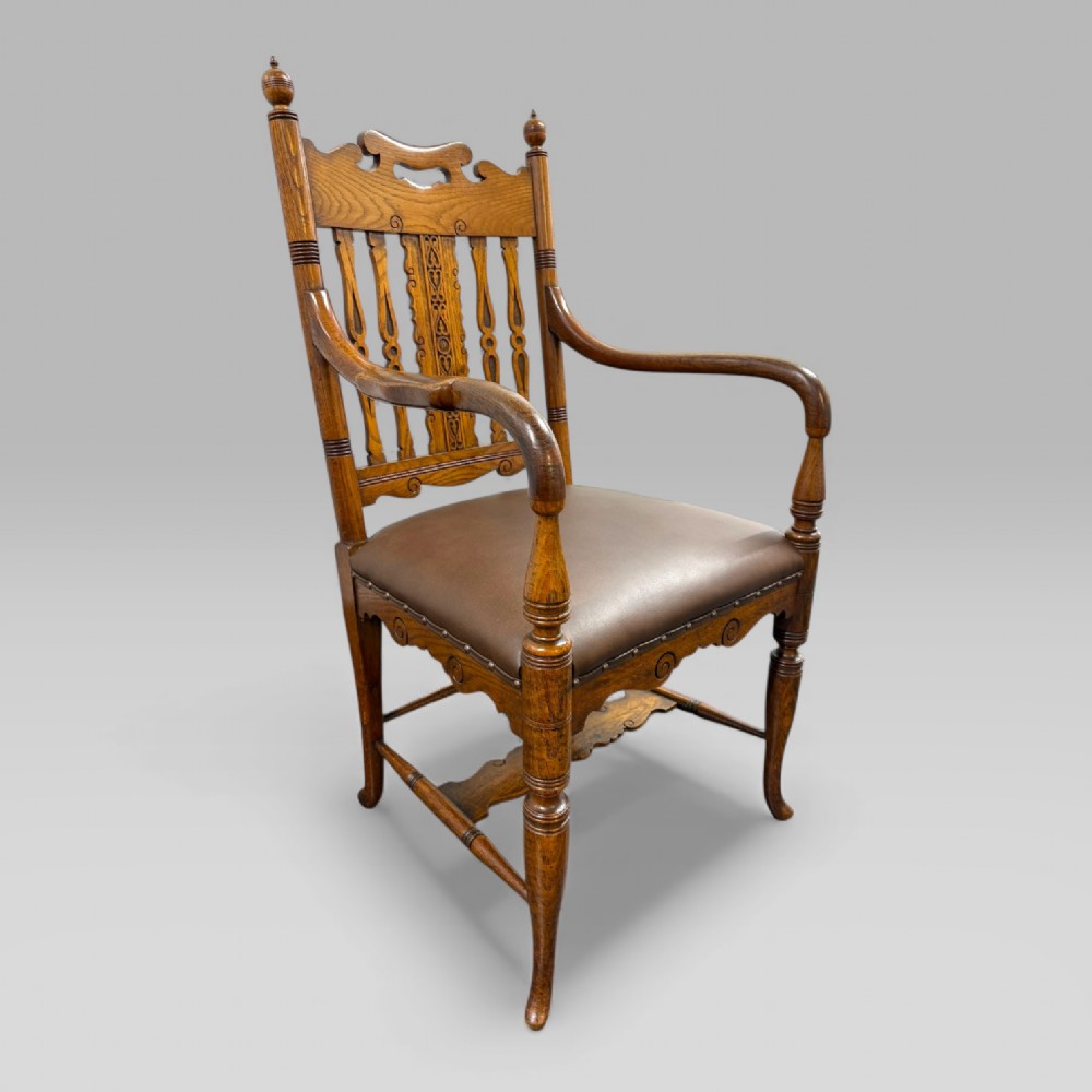 A Victorian carved golden oak armchair featuring a pierced vertical slat backrest, sculpted armrests, turned legs, and a brown leather seat. View III