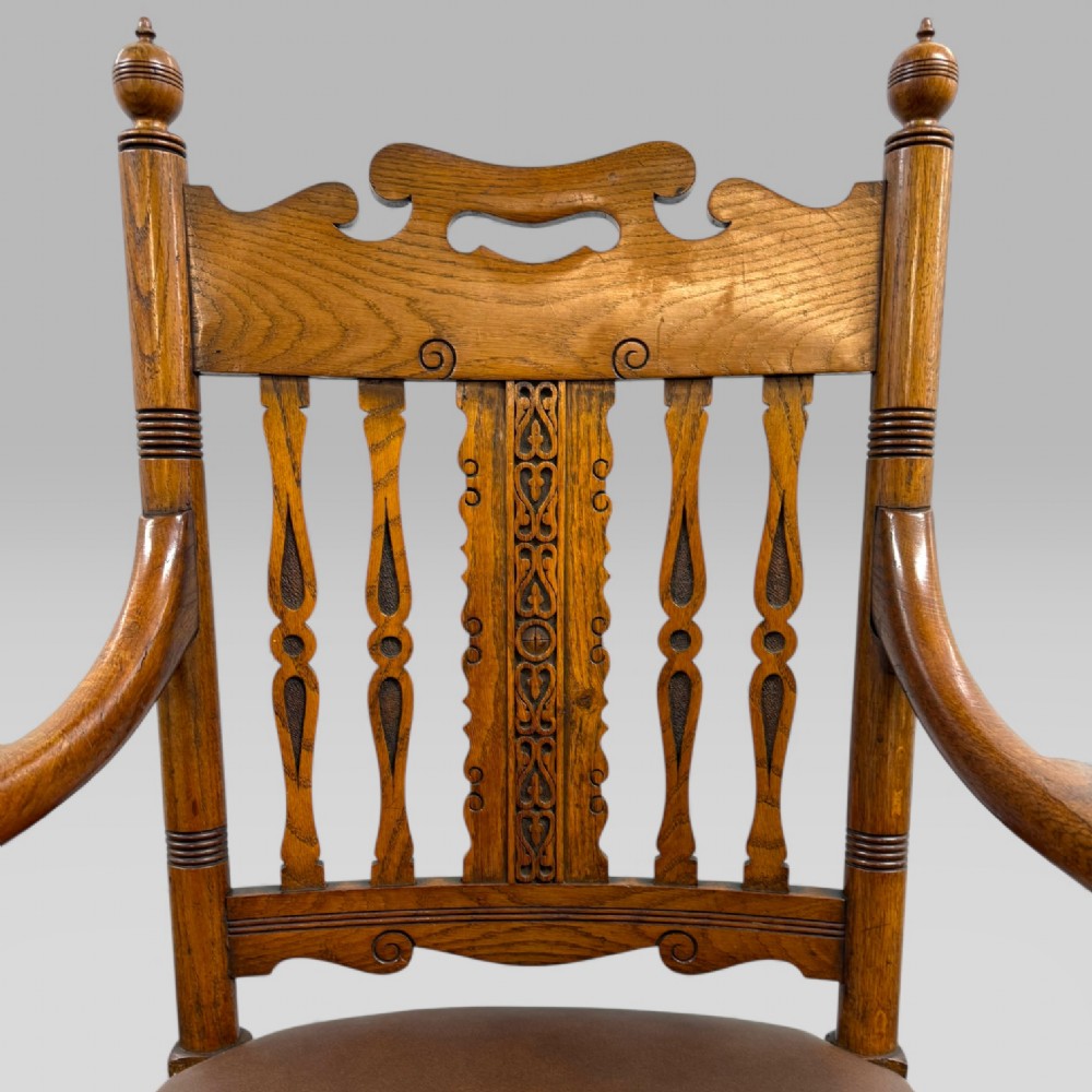 A Victorian carved golden oak armchair featuring a pierced vertical slat backrest, sculpted armrests, turned legs, and a brown leather seat. View IV