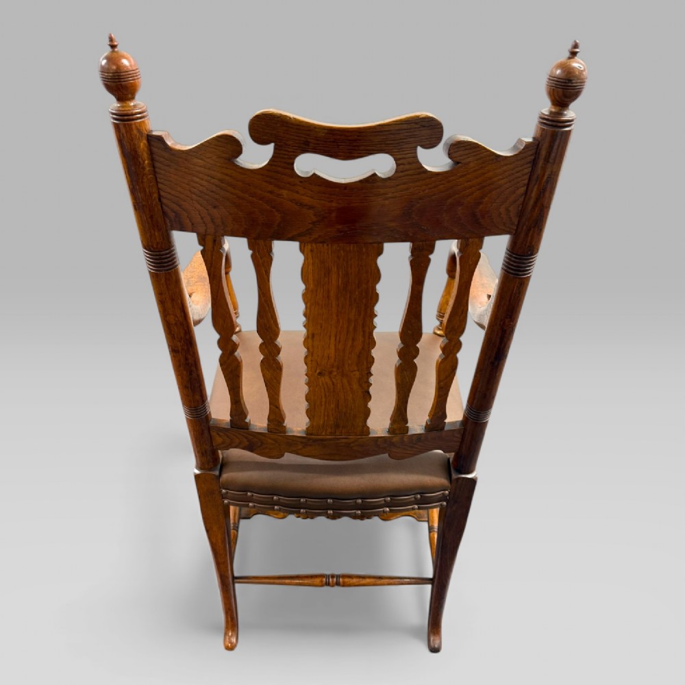 A Victorian carved golden oak armchair featuring a pierced vertical slat backrest, sculpted armrests, turned legs, and a brown leather seat. View V