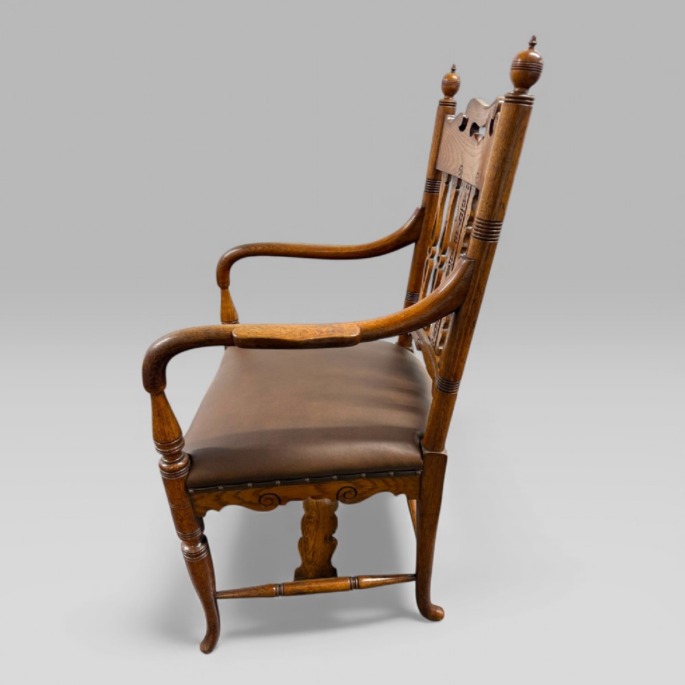 A Victorian carved golden oak armchair featuring a pierced vertical slat backrest, sculpted armrests, turned legs, and a brown leather seat. View VI