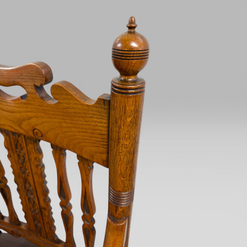 A Victorian carved golden oak armchair featuring a pierced vertical slat backrest, sculpted armrests, turned legs, and a brown leather seat. View VII