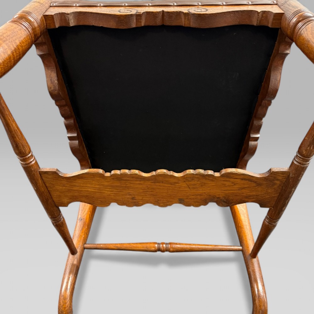 A Victorian carved golden oak armchair featuring a pierced vertical slat backrest, sculpted armrests, turned legs, and a brown leather seat. View XI