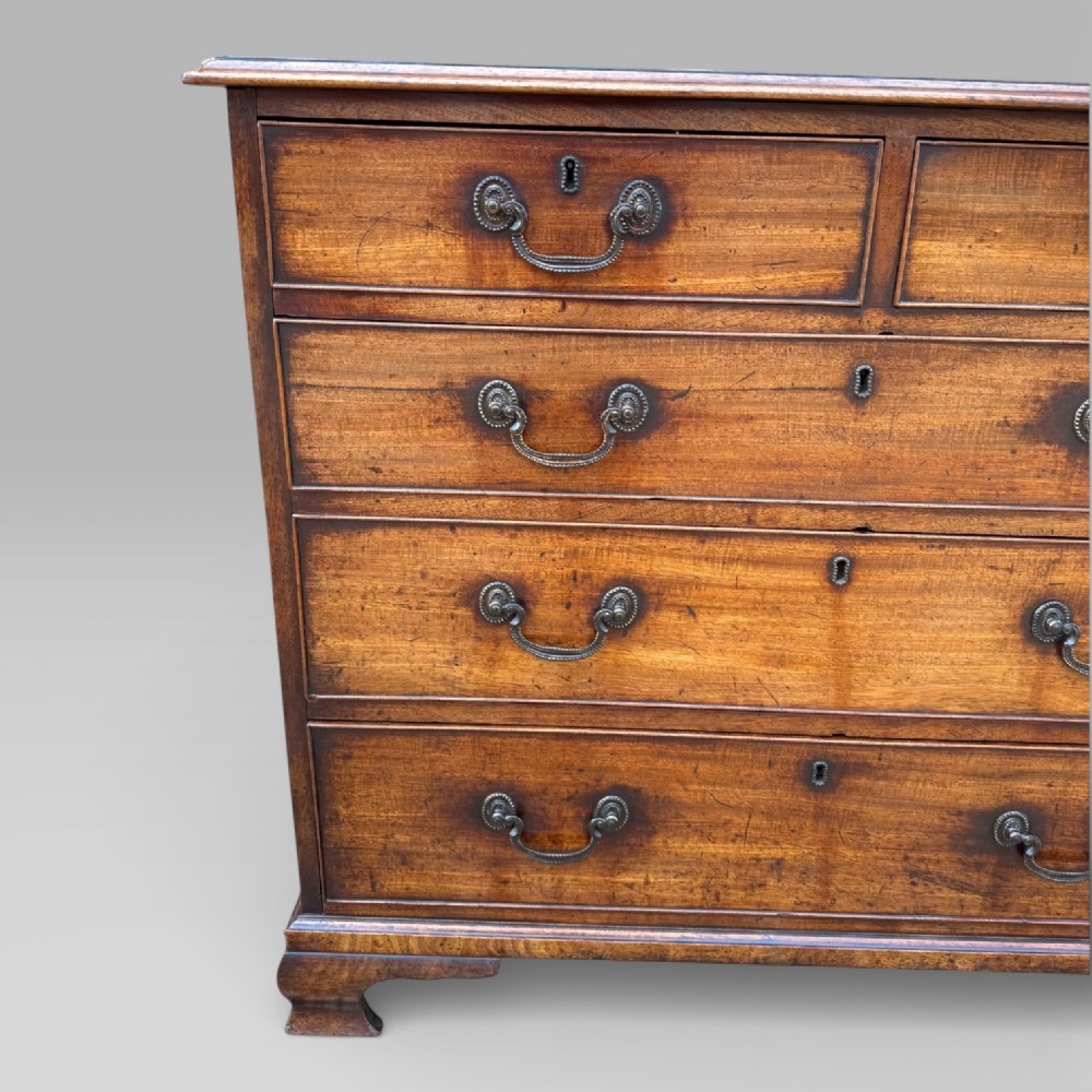 A late 18th-century George III mahogany chest of drawers featuring two short over three long drawers with brass swan-neck handles and bracket feet. View V
