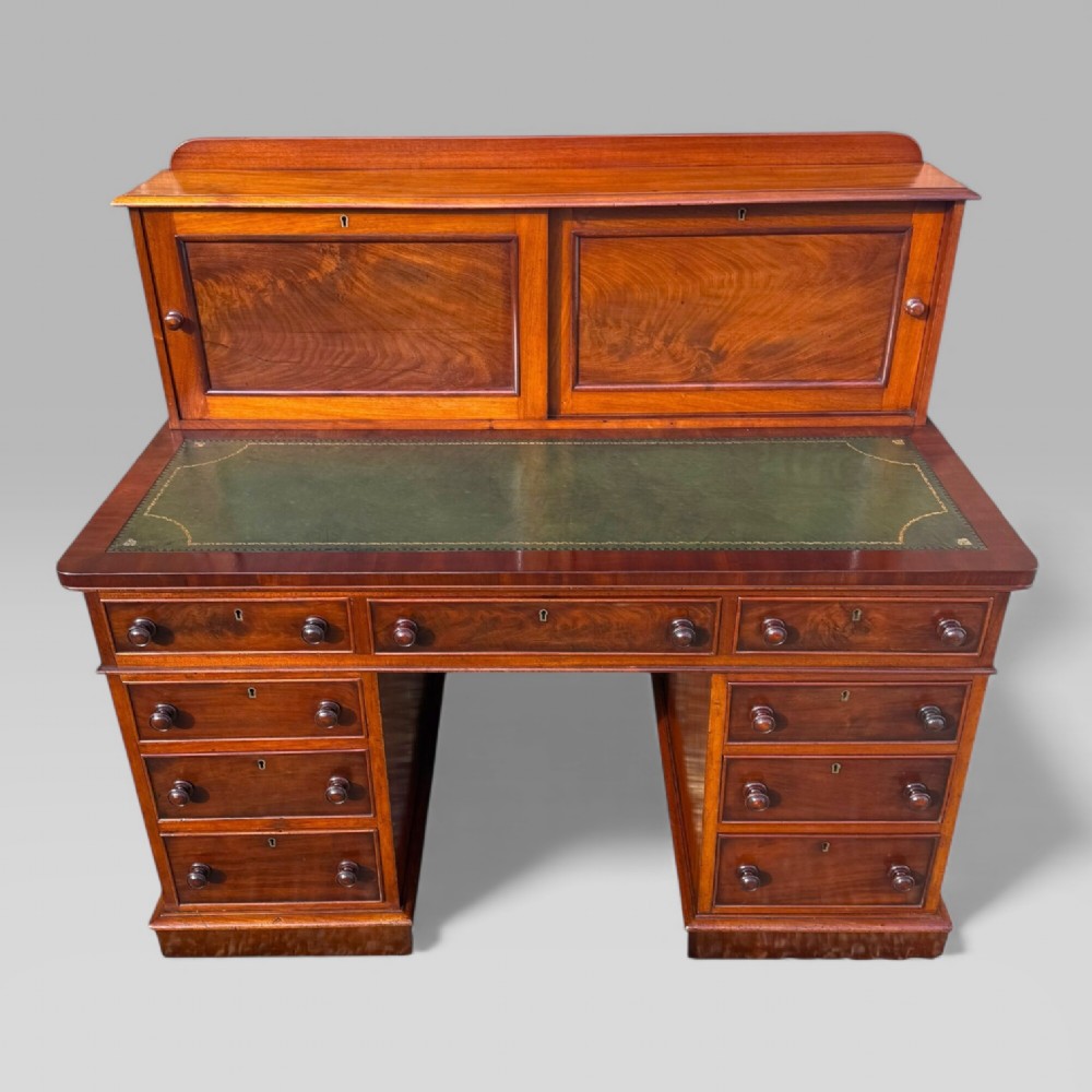 A Victorian mahogany pedestal desk featuring a green tooled leather writing surface, nine drawers with turned handles, and a raised upper cupboard superstructure.
