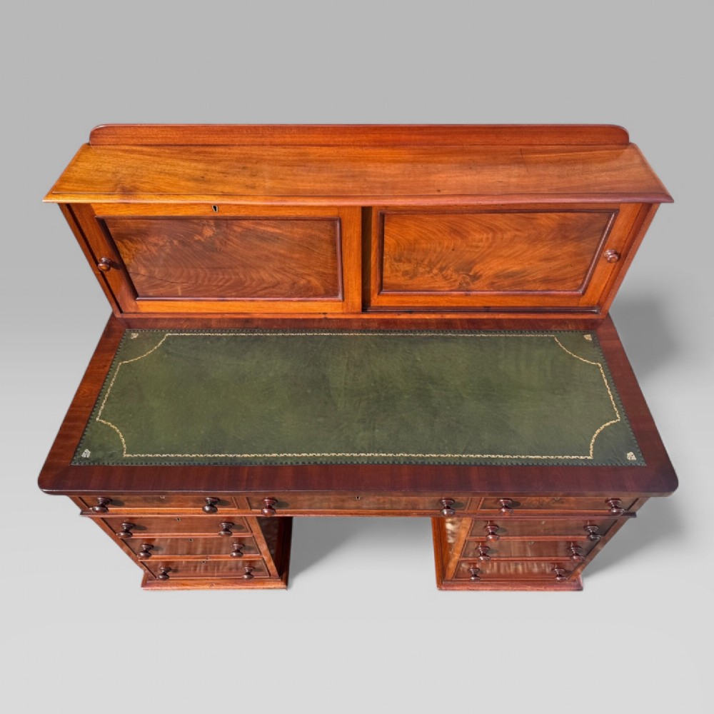A Victorian mahogany pedestal desk featuring a green tooled leather writing surface, nine drawers with turned handles, and a raised upper cupboard superstructure. View V