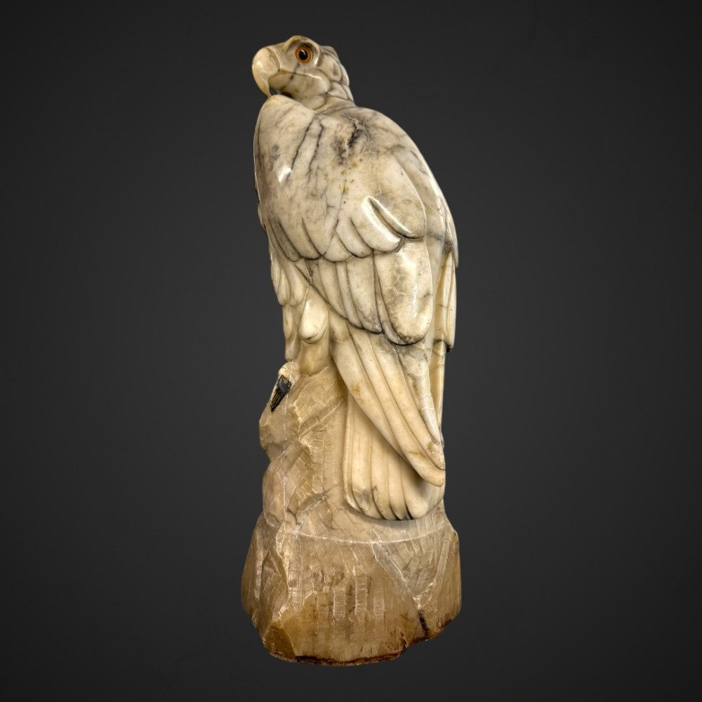 A 19th-century carved veined white marble eagle statue with amber glass eyes perched atop a rock formation. View III