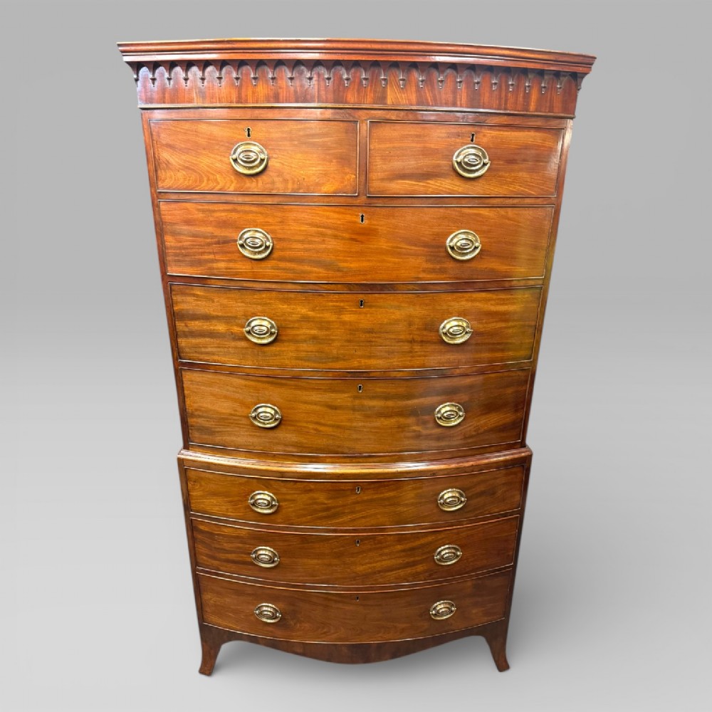 An antique Georgian mahogany bow-front chest on chest featuring two short over five long drawers with brass drop handles and an ornamental carved cornice.