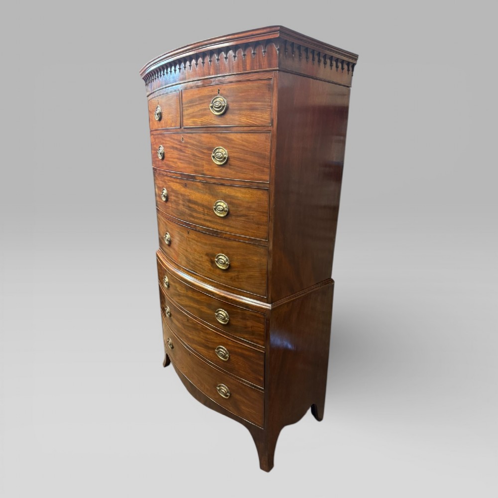 An antique Georgian mahogany bow-front chest on chest featuring two short over five long drawers with brass drop handles and an ornamental carved cornice. View II