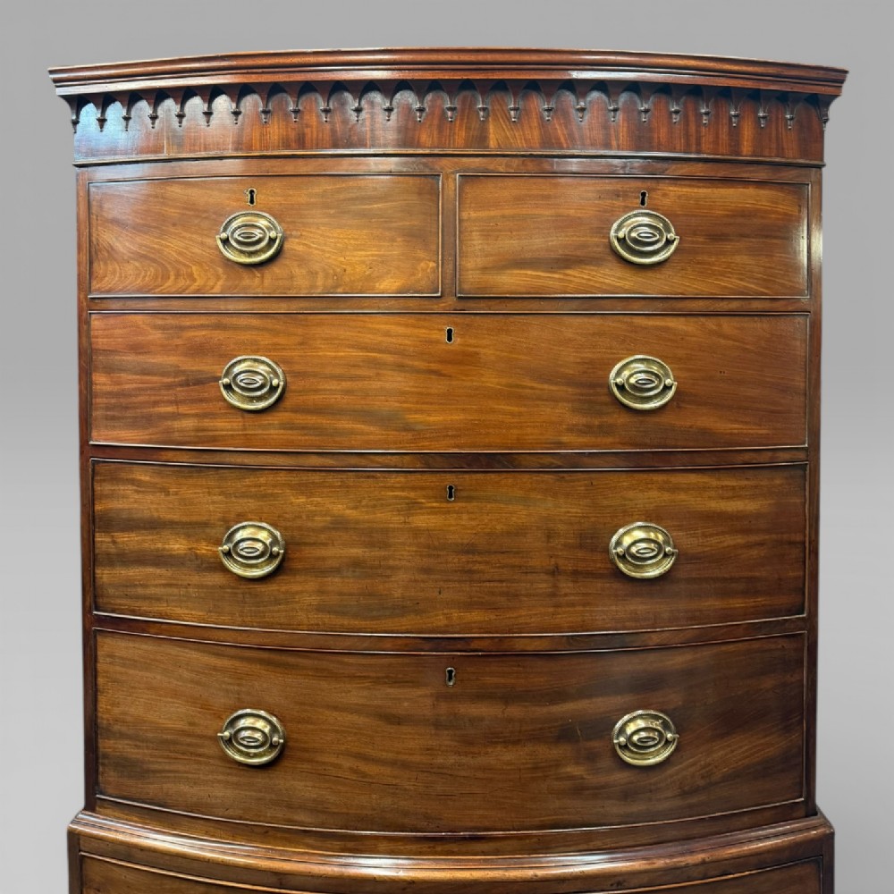 An antique Georgian mahogany bow-front chest on chest featuring two short over five long drawers with brass drop handles and an ornamental carved cornice. View IV