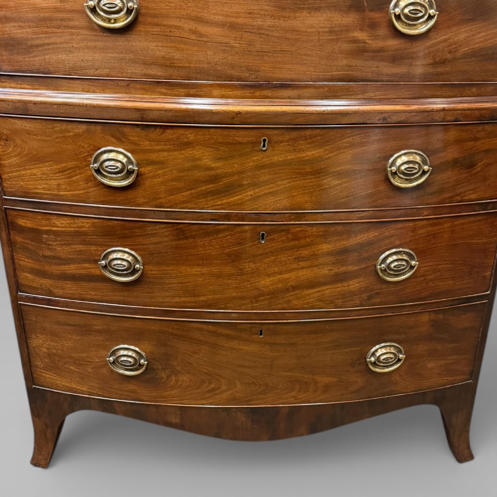An antique Georgian mahogany bow-front chest on chest featuring two short over five long drawers with brass drop handles and an ornamental carved cornice. View V
