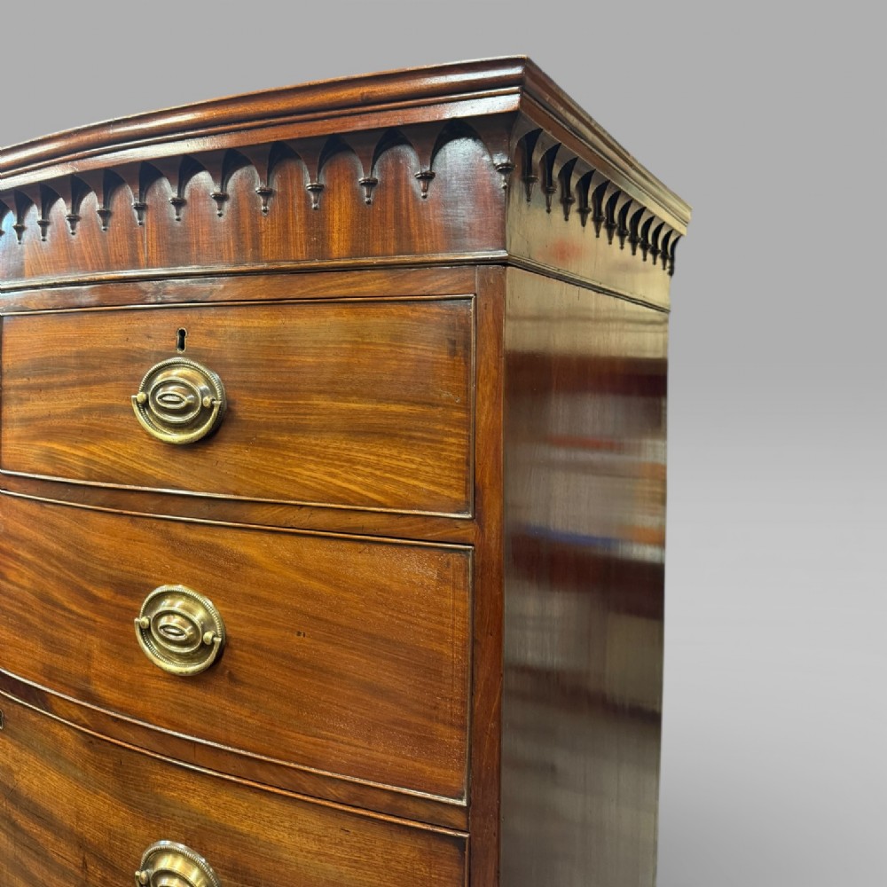 An antique Georgian mahogany bow-front chest on chest featuring two short over five long drawers with brass drop handles and an ornamental carved cornice. View VI