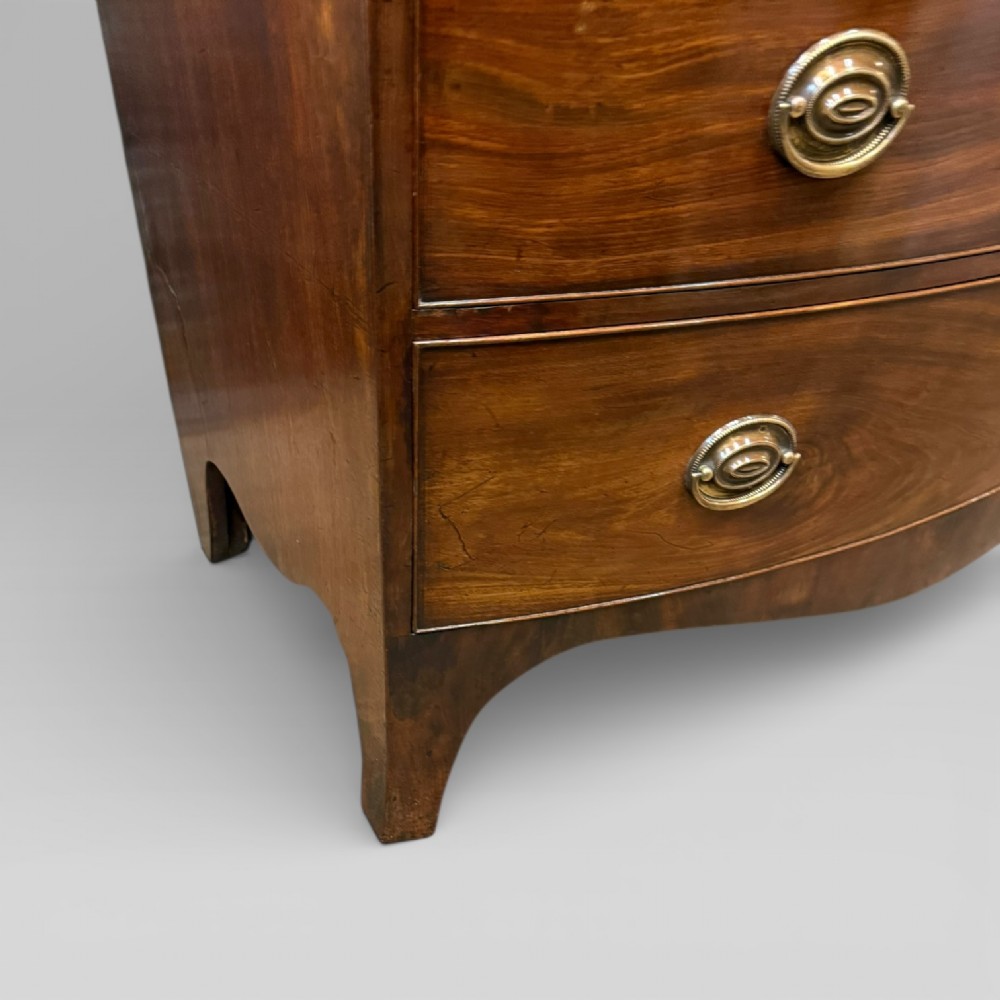 An antique Georgian mahogany bow-front chest on chest featuring two short over five long drawers with brass drop handles and an ornamental carved cornice. View VII