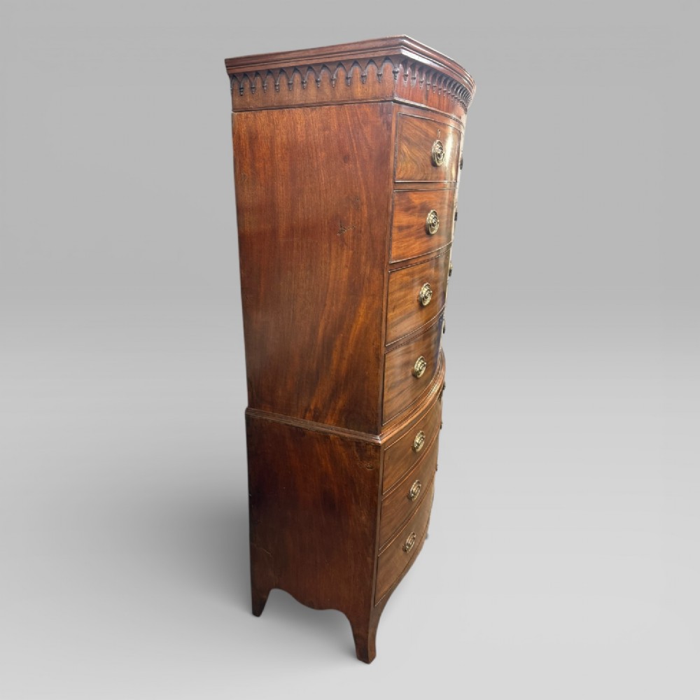 An antique Georgian mahogany bow-front chest on chest featuring two short over five long drawers with brass drop handles and an ornamental carved cornice. View VIII