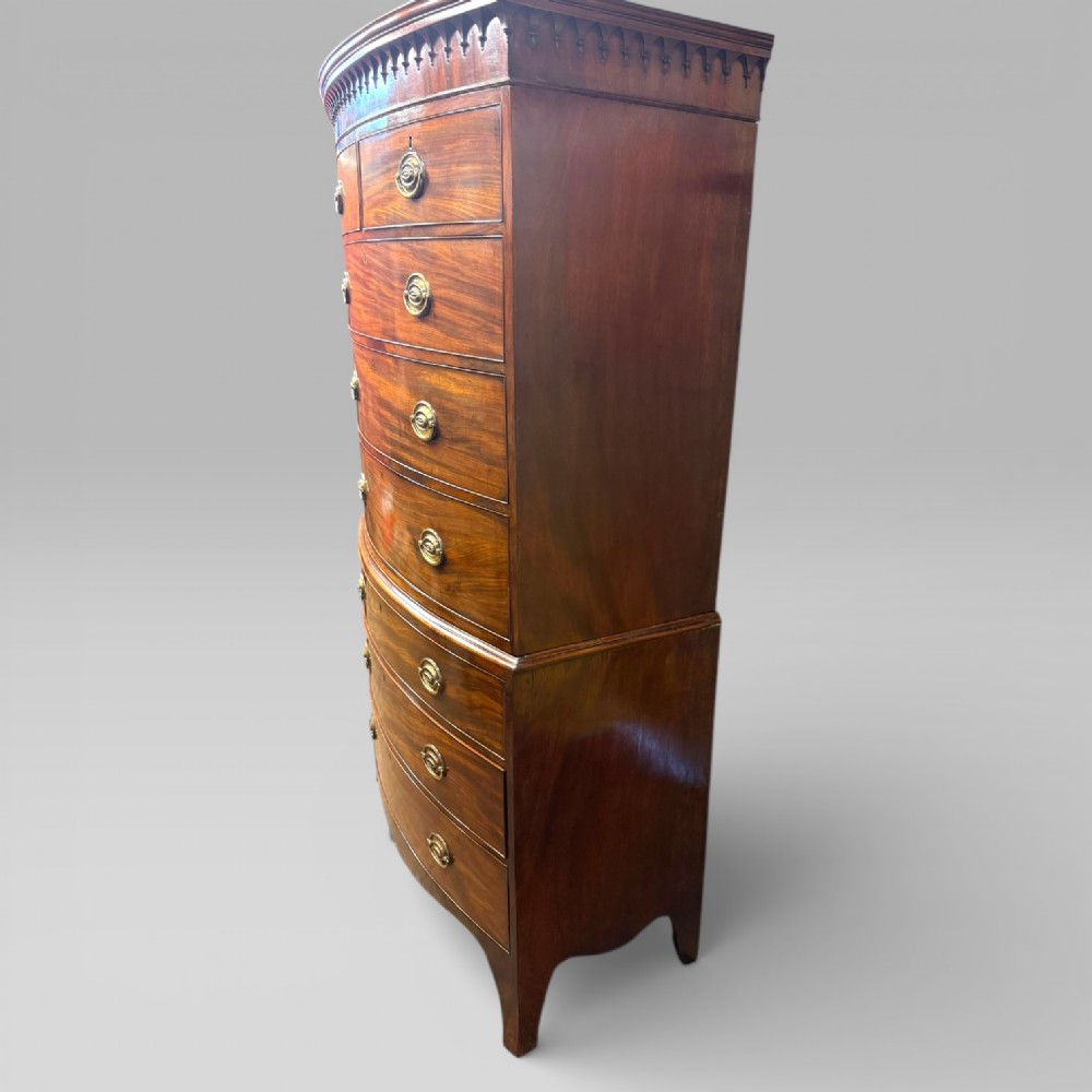 An antique Georgian mahogany bow-front chest on chest featuring two short over five long drawers with brass drop handles and an ornamental carved cornice. View IX