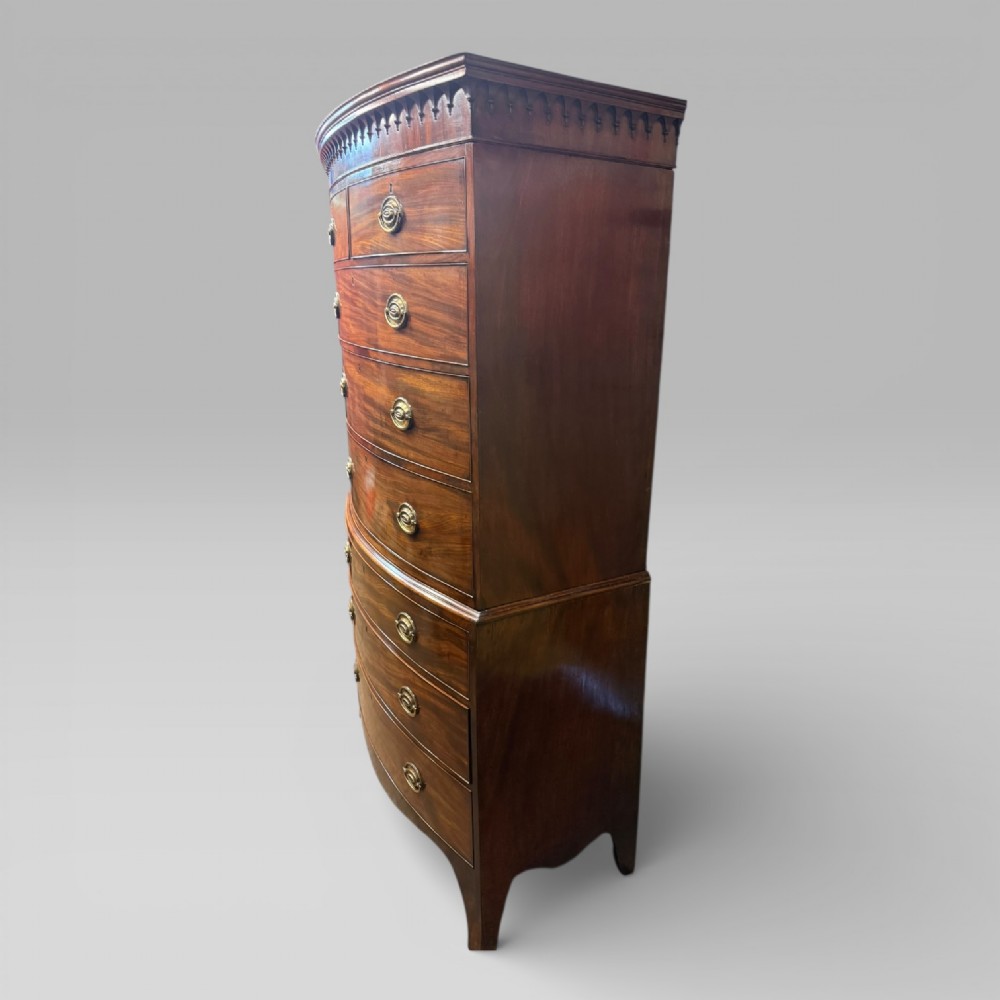 An antique Georgian mahogany bow-front chest on chest featuring two short over five long drawers with brass drop handles and an ornamental carved cornice. View X