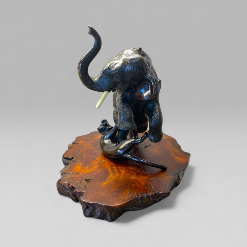 A dark patinated bronze sculpture depicting an elephant defending itself against two tigers, mounted on a polished natural edge wooden base. View IV