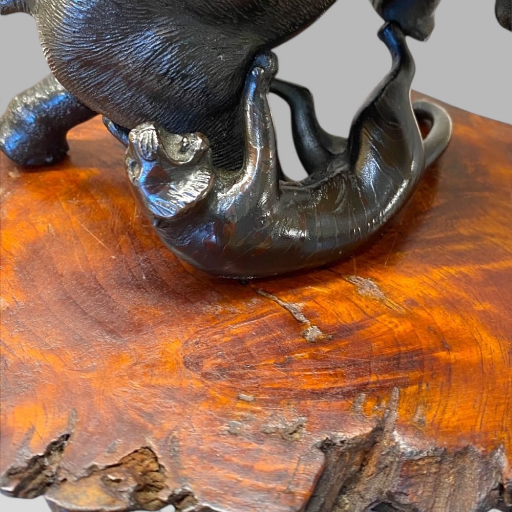 A dark patinated bronze sculpture depicting an elephant defending itself against two tigers, mounted on a polished natural edge wooden base. View V