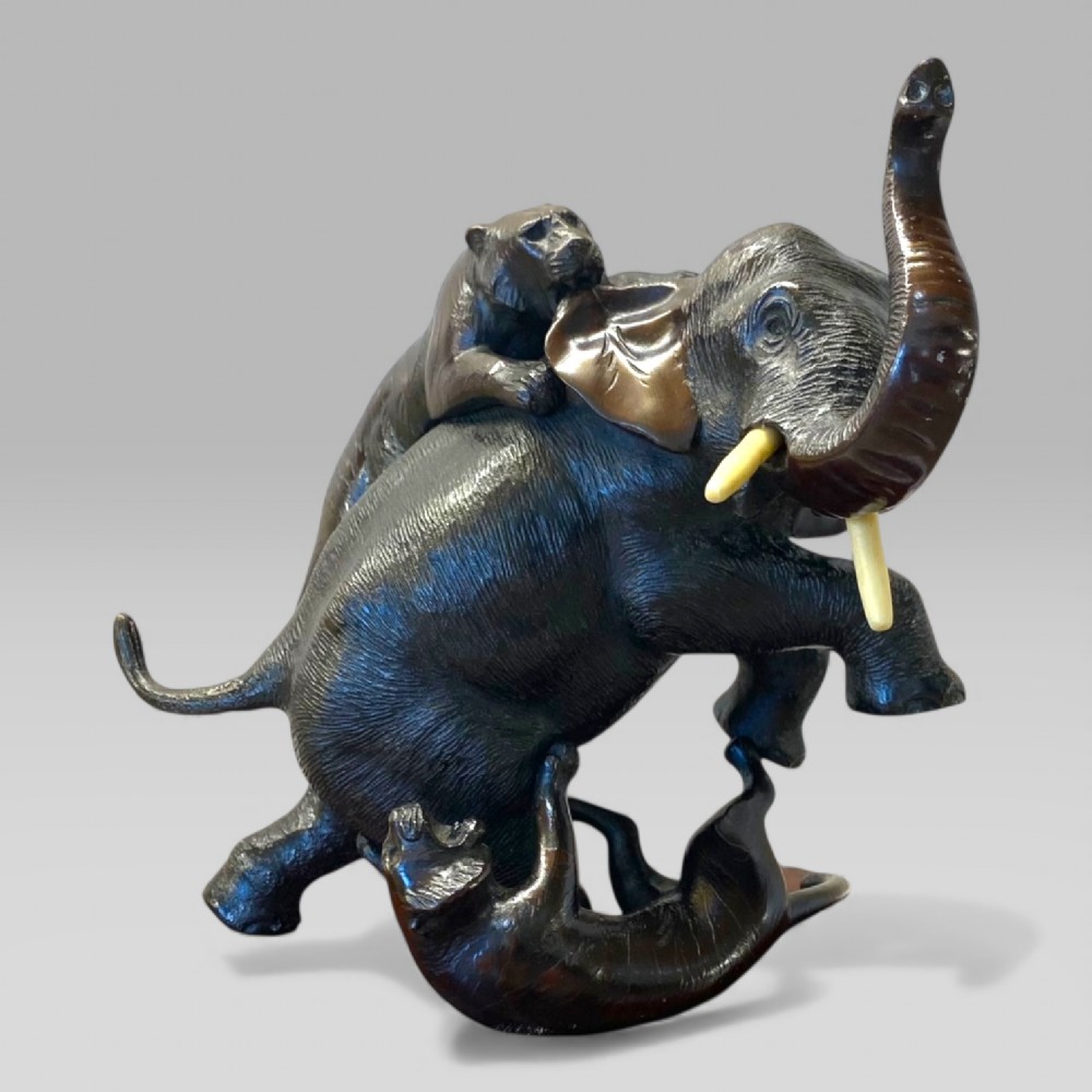 A dark patinated bronze sculpture depicting an elephant defending itself against two tigers, mounted on a polished natural edge wooden base. View VI