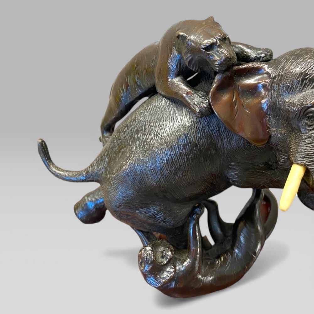 A dark patinated bronze sculpture depicting an elephant defending itself against two tigers, mounted on a polished natural edge wooden base. View VII