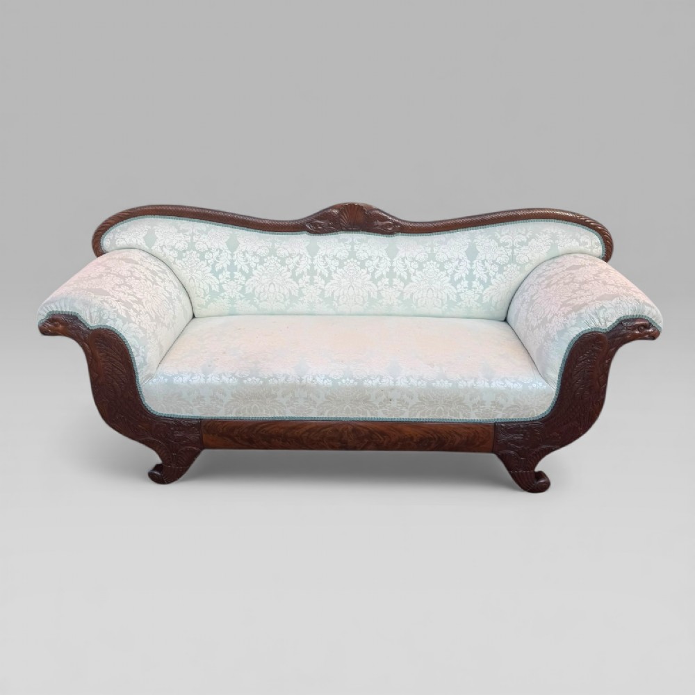 A nineteenth-century French Empire flame mahogany sofa featuring carved scroll arms, a serpentine crest, and light blue damask fabric upholstery.