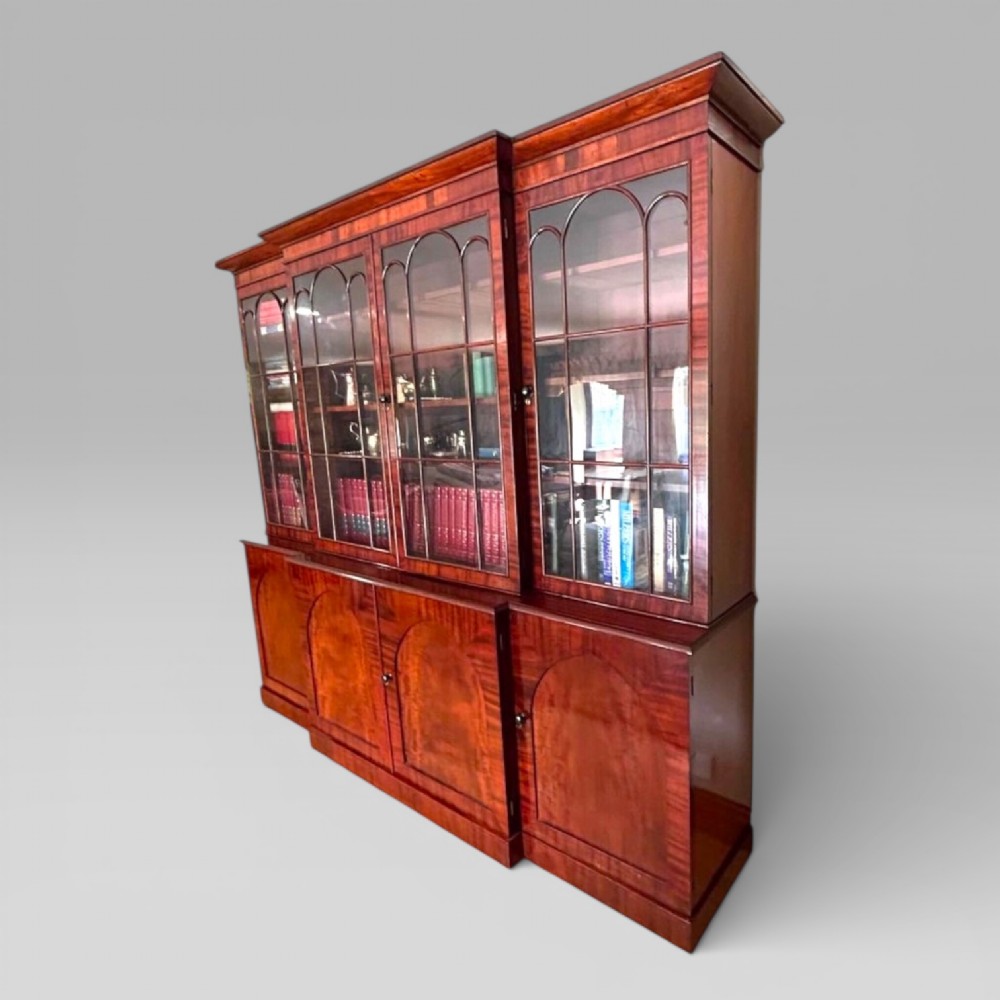 A large William IV flame mahogany breakfront library bookcase featuring four glazed upper doors with arched astragal glazing and four panelled cupboard doors beneath. View II