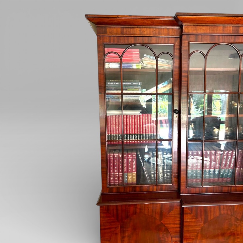 A large William IV flame mahogany breakfront library bookcase featuring four glazed upper doors with arched astragal glazing and four panelled cupboard doors beneath. View IV