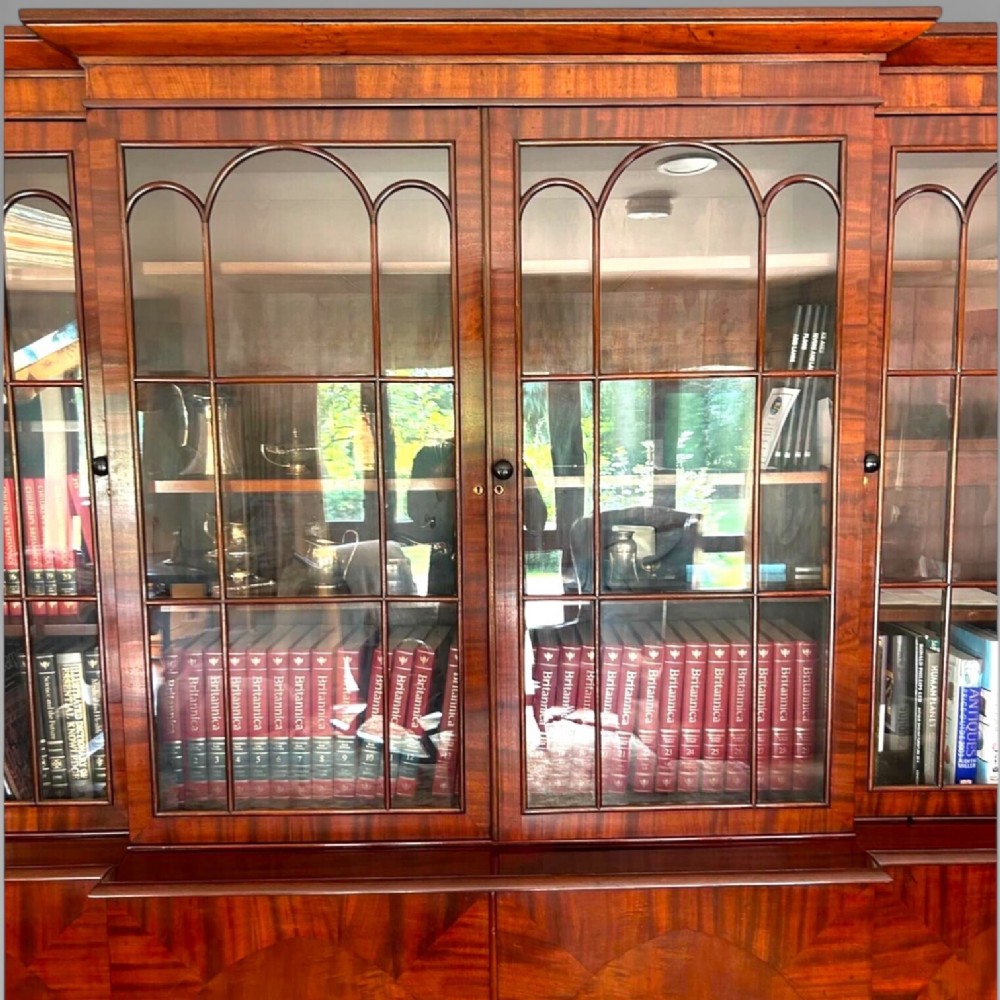 A large William IV flame mahogany breakfront library bookcase featuring four glazed upper doors with arched astragal glazing and four panelled cupboard doors beneath. View V