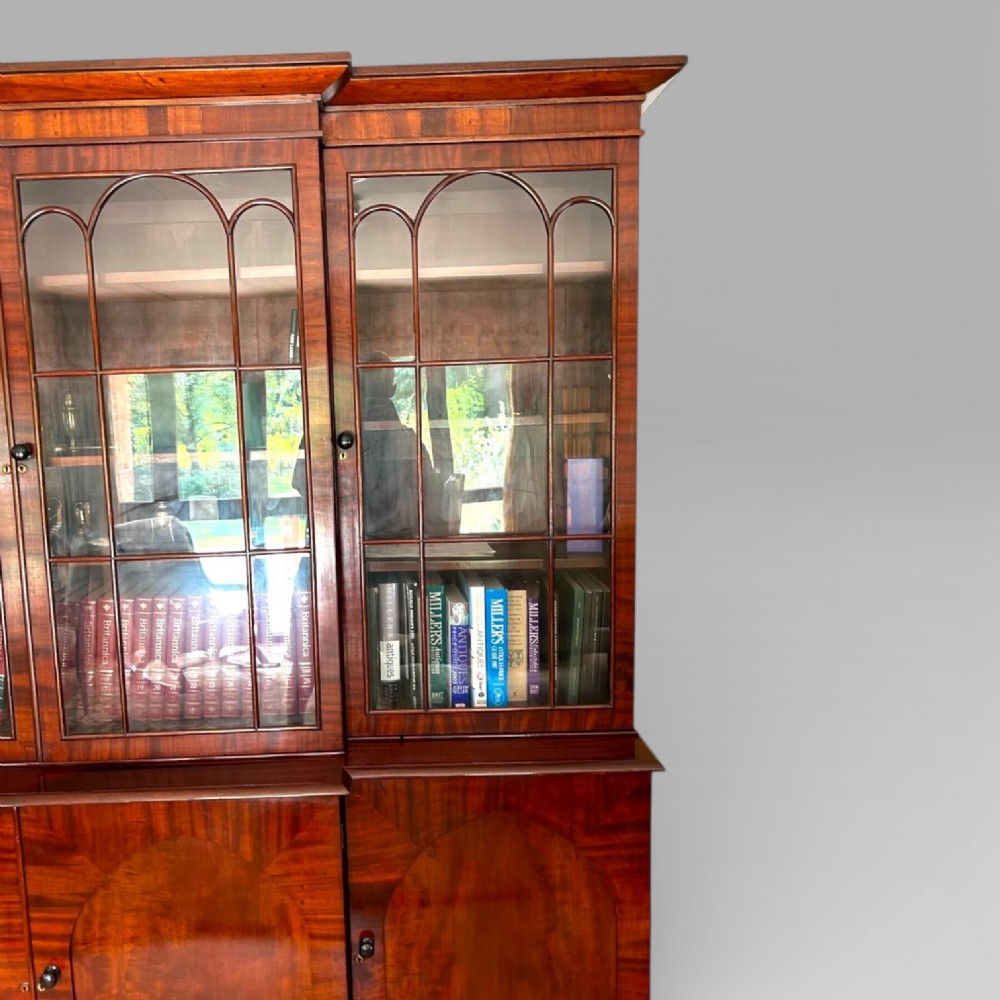 A large William IV flame mahogany breakfront library bookcase featuring four glazed upper doors with arched astragal glazing and four panelled cupboard doors beneath. View VI