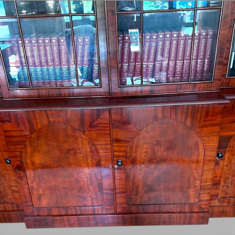 A large William IV flame mahogany breakfront library bookcase featuring four glazed upper doors with arched astragal glazing and four panelled cupboard doors beneath. View VII