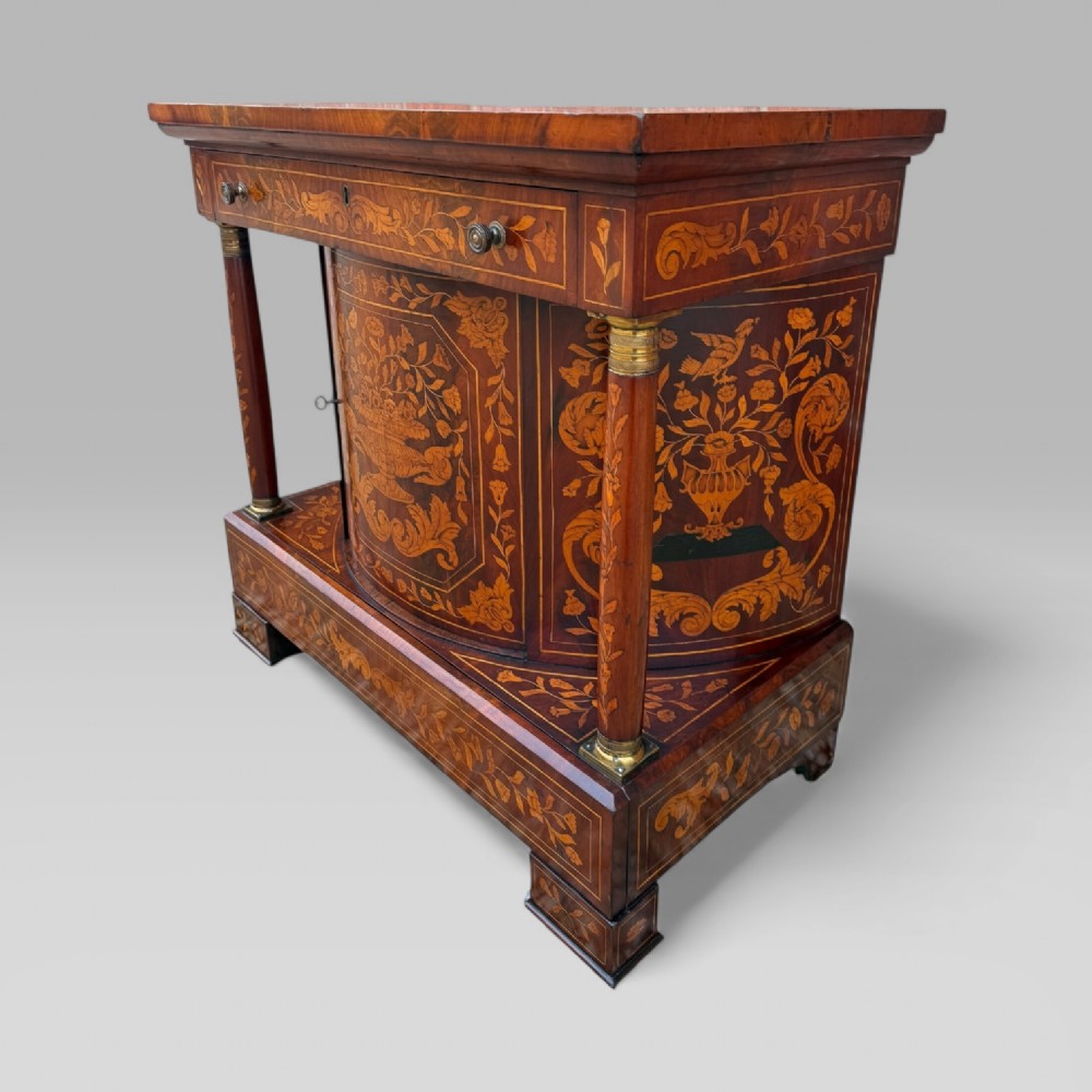 An 18th-century Dutch mahogany console table cabinet featuring detailed floral marquetry inlay, twin supporting columns, and a central cupboard door on a plinth base. View III