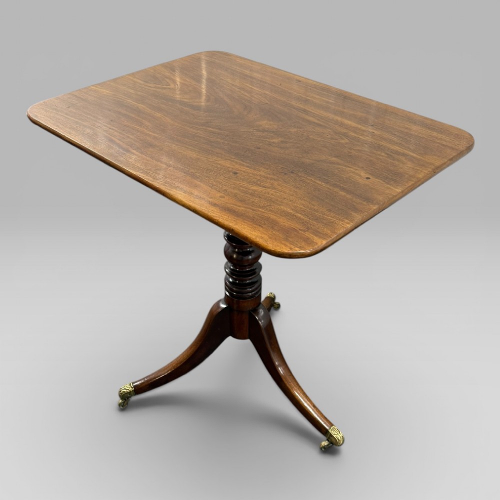 A Regency mahogany tilt-top table featuring a rectangular surface, turned central pedestal column, and tripod splayed legs with brass lion paw castors. View III