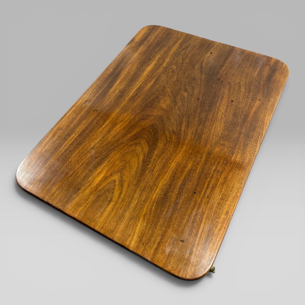 A Regency mahogany tilt-top table featuring a rectangular surface, turned central pedestal column, and tripod splayed legs with brass lion paw castors. View VI