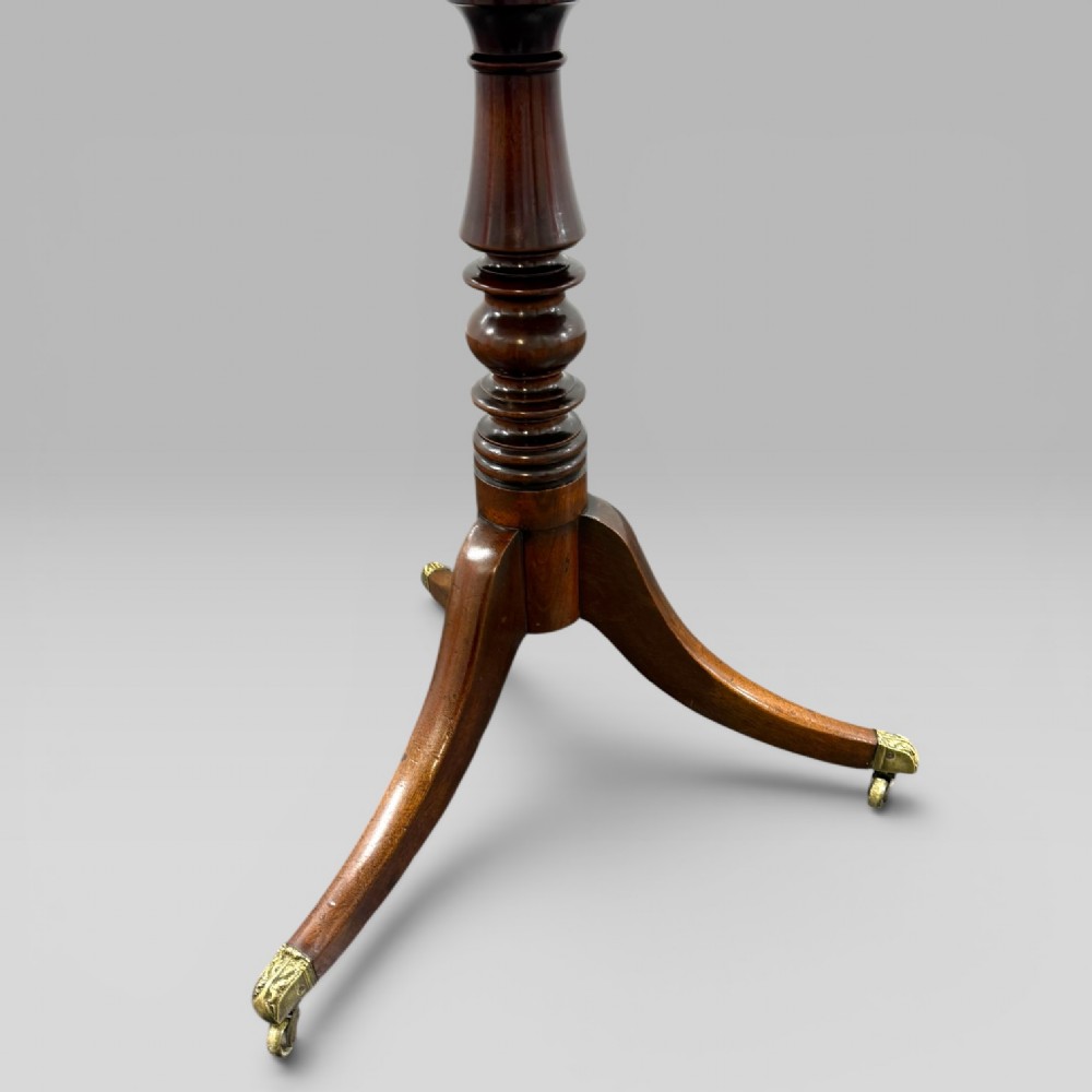 A Regency mahogany tilt-top table featuring a rectangular surface, turned central pedestal column, and tripod splayed legs with brass lion paw castors. View VII