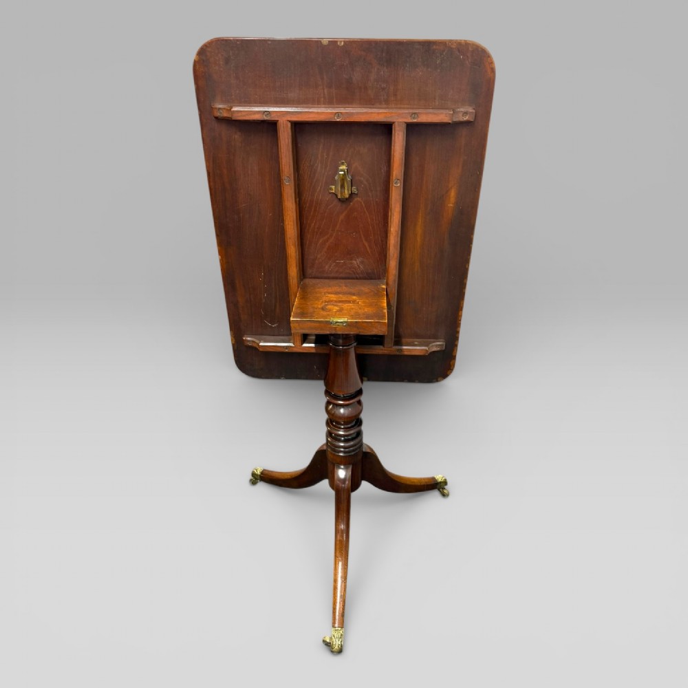 A Regency mahogany tilt-top table featuring a rectangular surface, turned central pedestal column, and tripod splayed legs with brass lion paw castors. View VIII