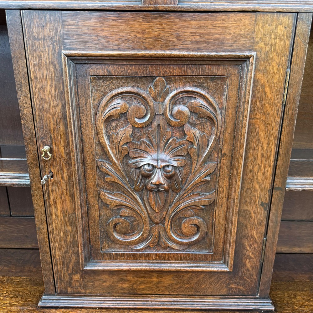 A late Victorian dark oak dresser with carved Green Man foliate motifs on the cupboard doors, open display shelving, and cabriole legs. View IV