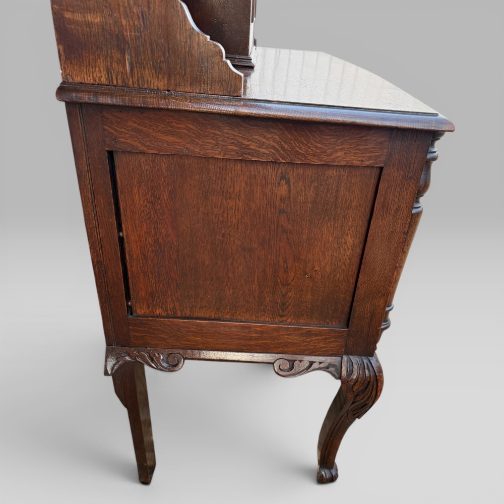 A late Victorian dark oak dresser with carved Green Man foliate motifs on the cupboard doors, open display shelving, and cabriole legs. View VII