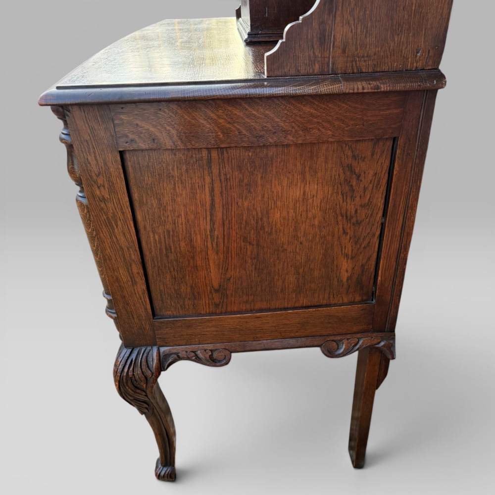 A late Victorian dark oak dresser with carved Green Man foliate motifs on the cupboard doors, open display shelving, and cabriole legs. View VIII