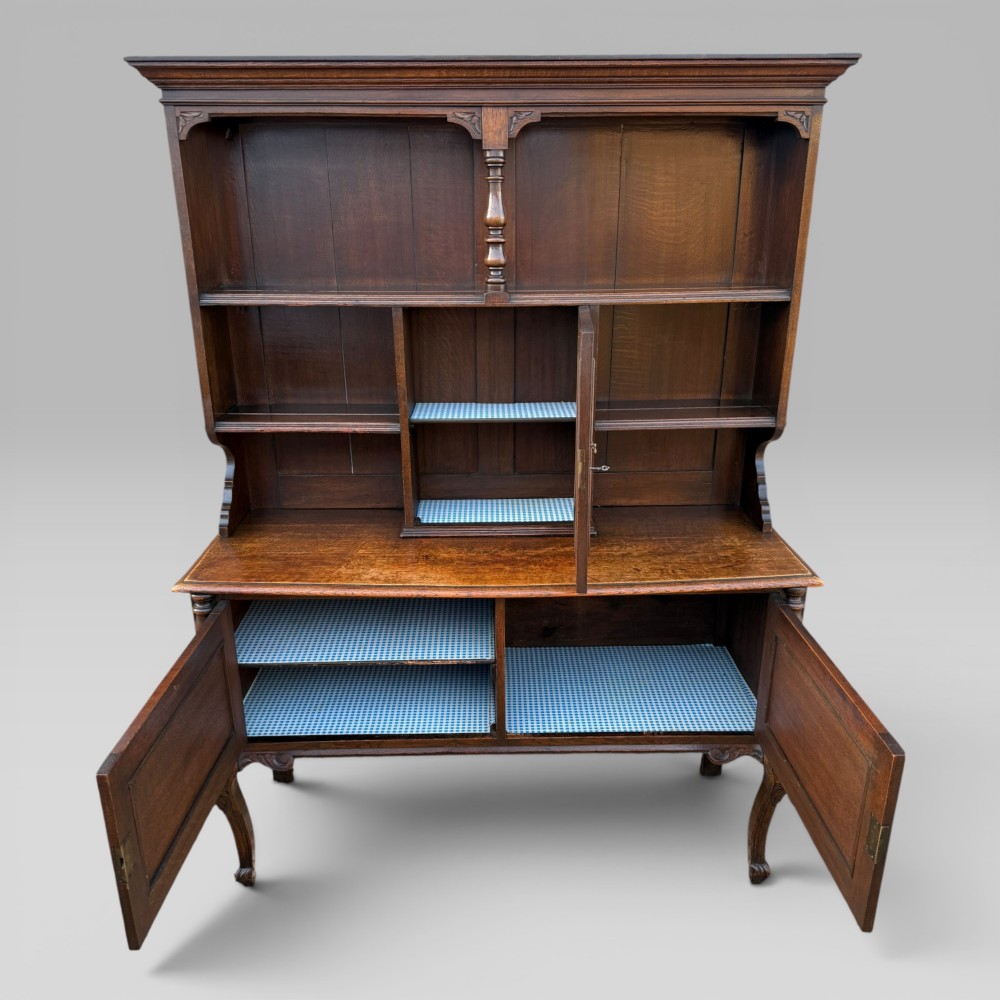 A late Victorian dark oak dresser with carved Green Man foliate motifs on the cupboard doors, open display shelving, and cabriole legs. View IX
