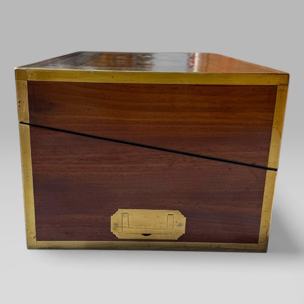 A rectangular dark timber writing slope featuring brass edge binding, intricate brass foliate inlay, a central brass nameplate, and a brass keyhole escutcheon. View V