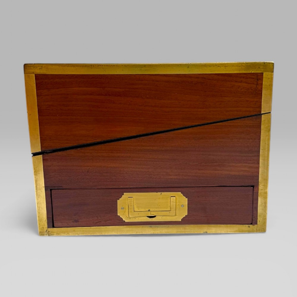 A rectangular dark timber writing slope featuring brass edge binding, intricate brass foliate inlay, a central brass nameplate, and a brass keyhole escutcheon. View VI